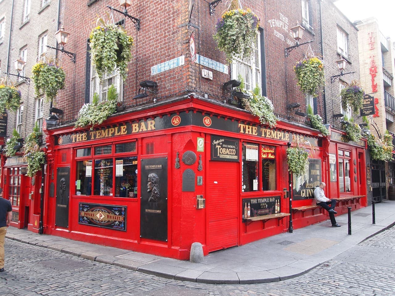 The red exterior of the Temple Bar pub in Dublin, decorated with hanging flower baskets and surrounded by cobbled streets.