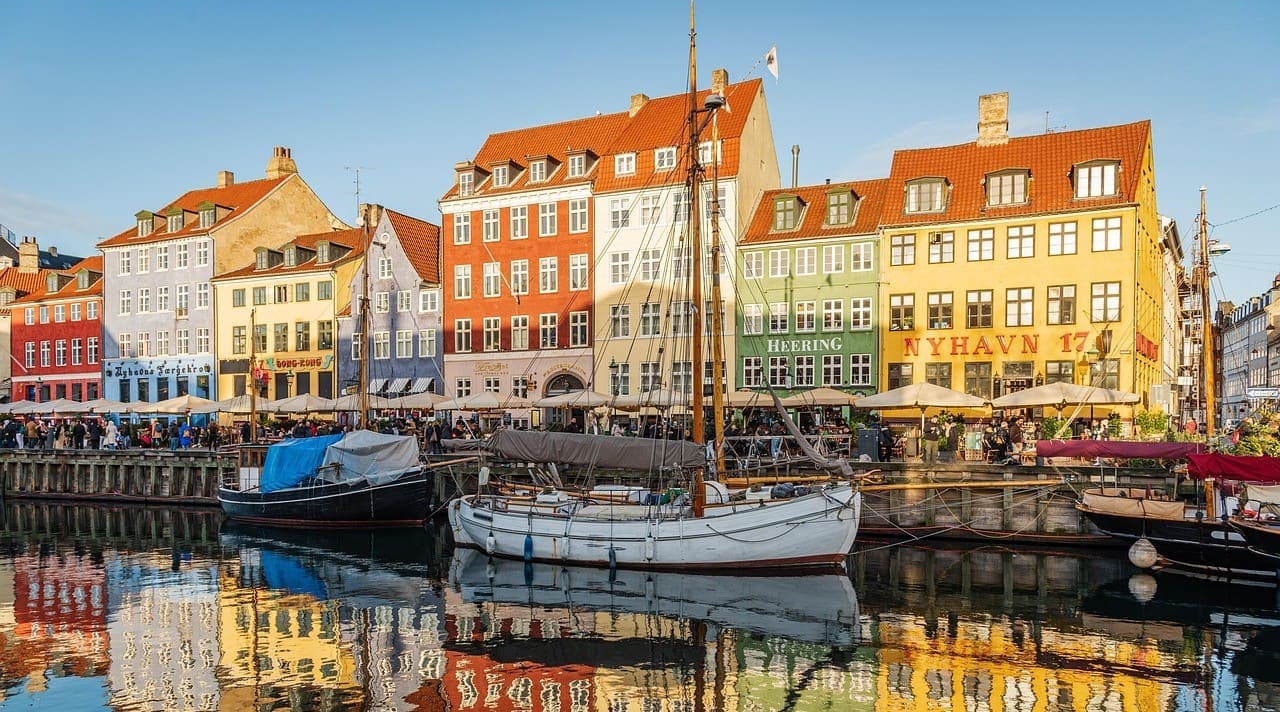 Colourful houses along the Nyhavn canal in Copenhagen with boats in the harbour and reflections in the water on a bright day.