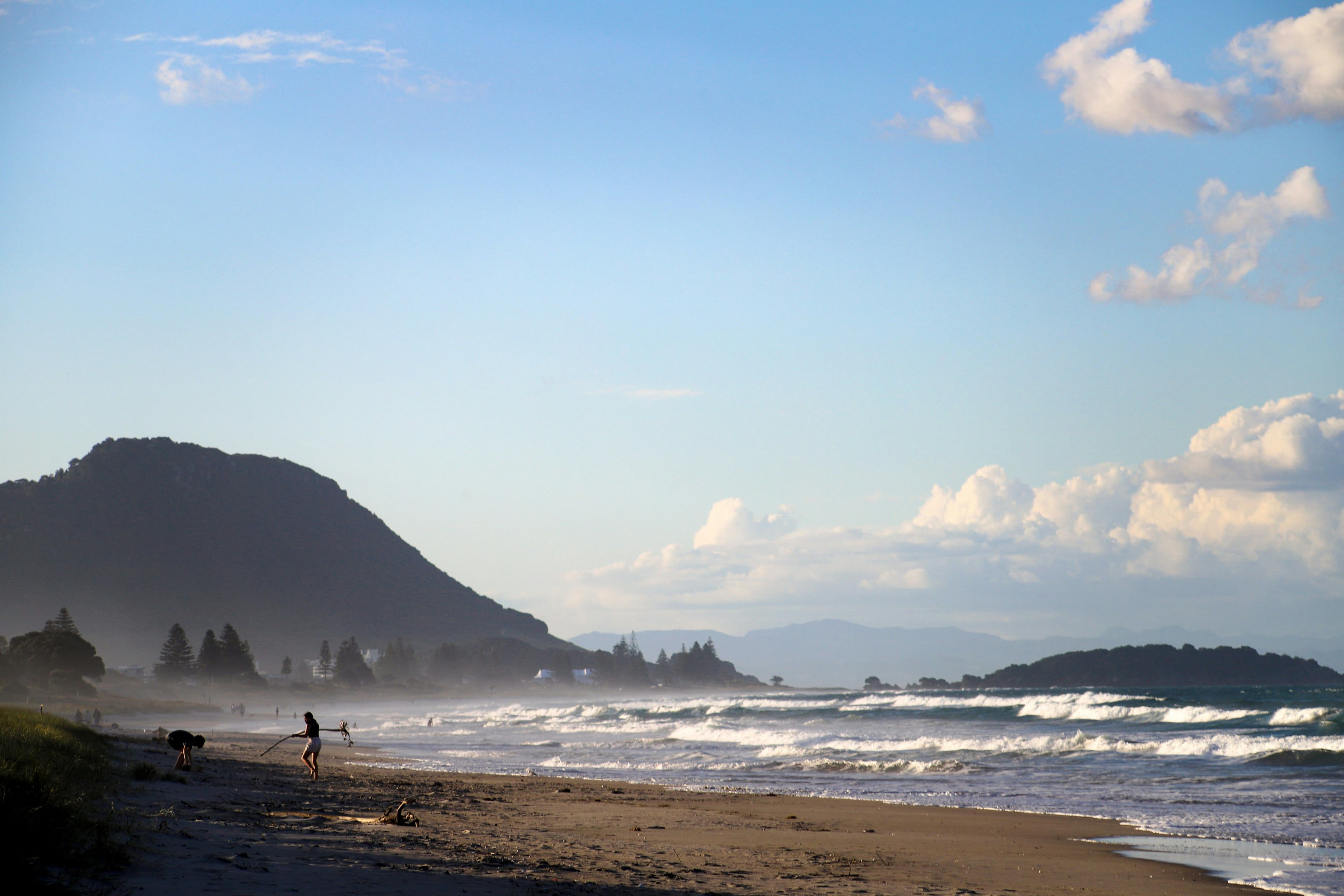 Piha Beach, a beach in new zealand with a mountain on the left and the ocean on the right on a cloudy day