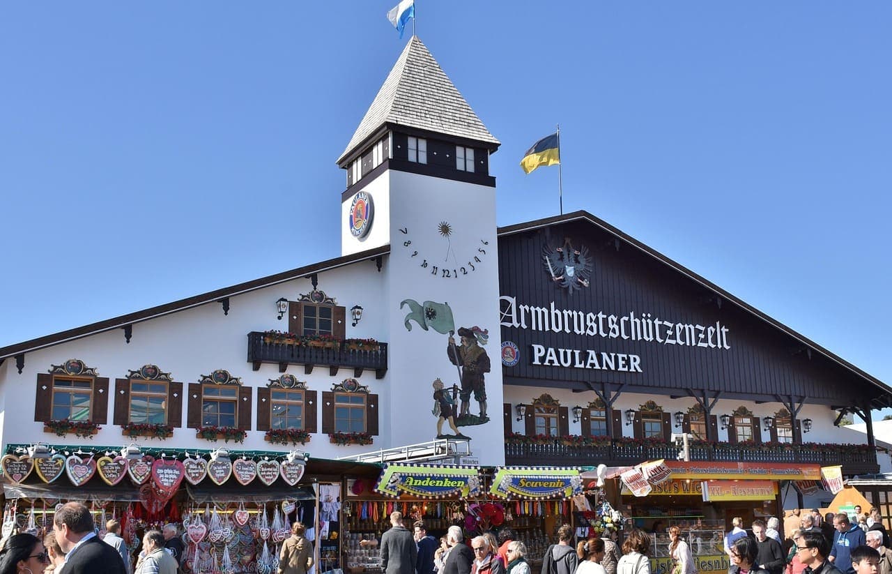 A large Oktoberfest beer tent in Munich filled with people standing outside under a blue sky.