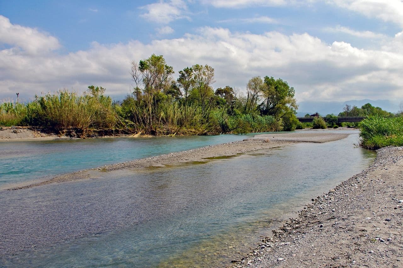 Shallow river landscape in southern Laos with sandbanks, small islands and trees under a bright blue sky.