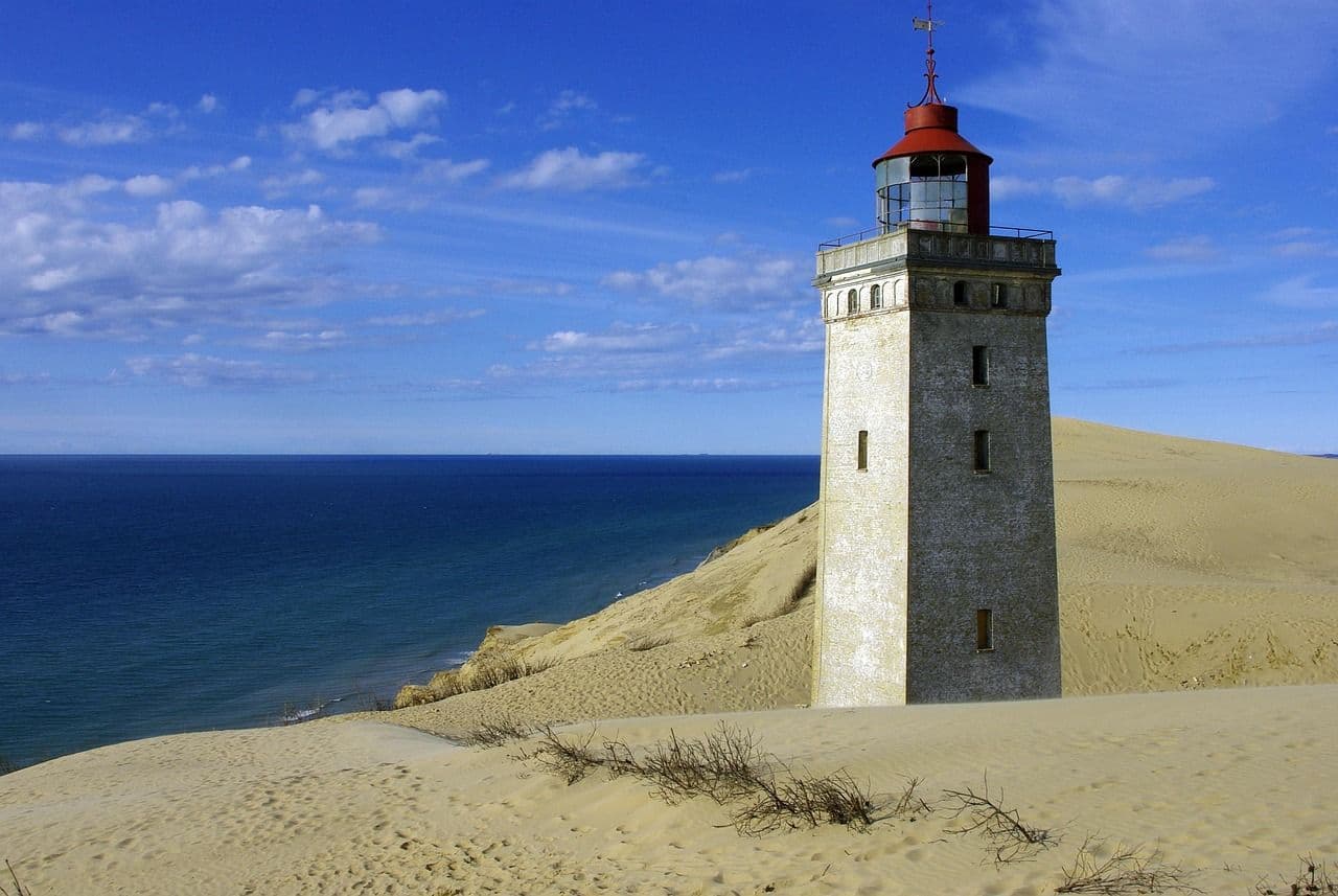 A lighthouse standing on sandy cliffs by the sea at Rubjerg Knude, with wide views over the coastline and dunes.