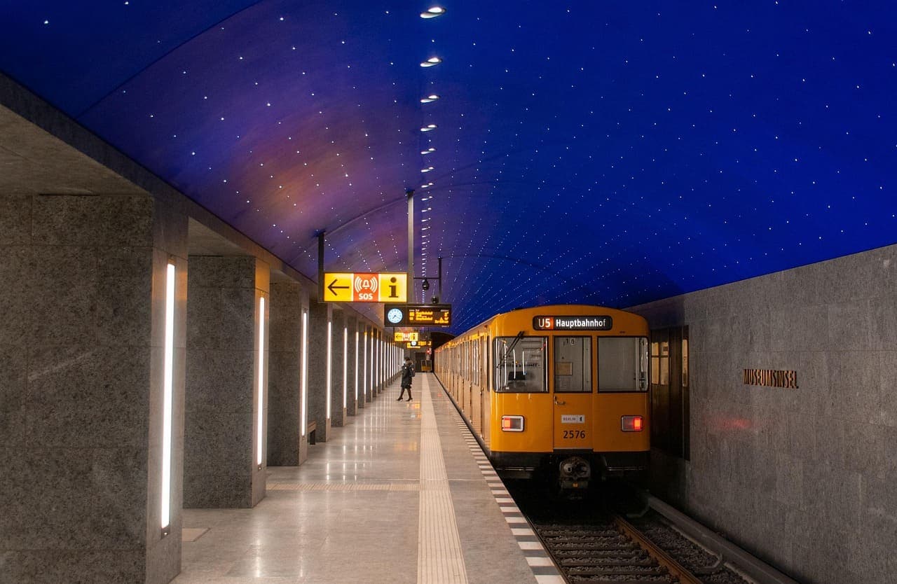 A Berlin underground train at a modern metro station platform with blue ceiling lights and clear signage.