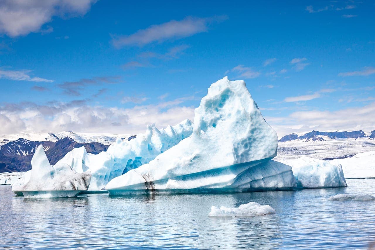Large blue iceberg floating in a glacier lagoon in Iceland with mountains in the distance.