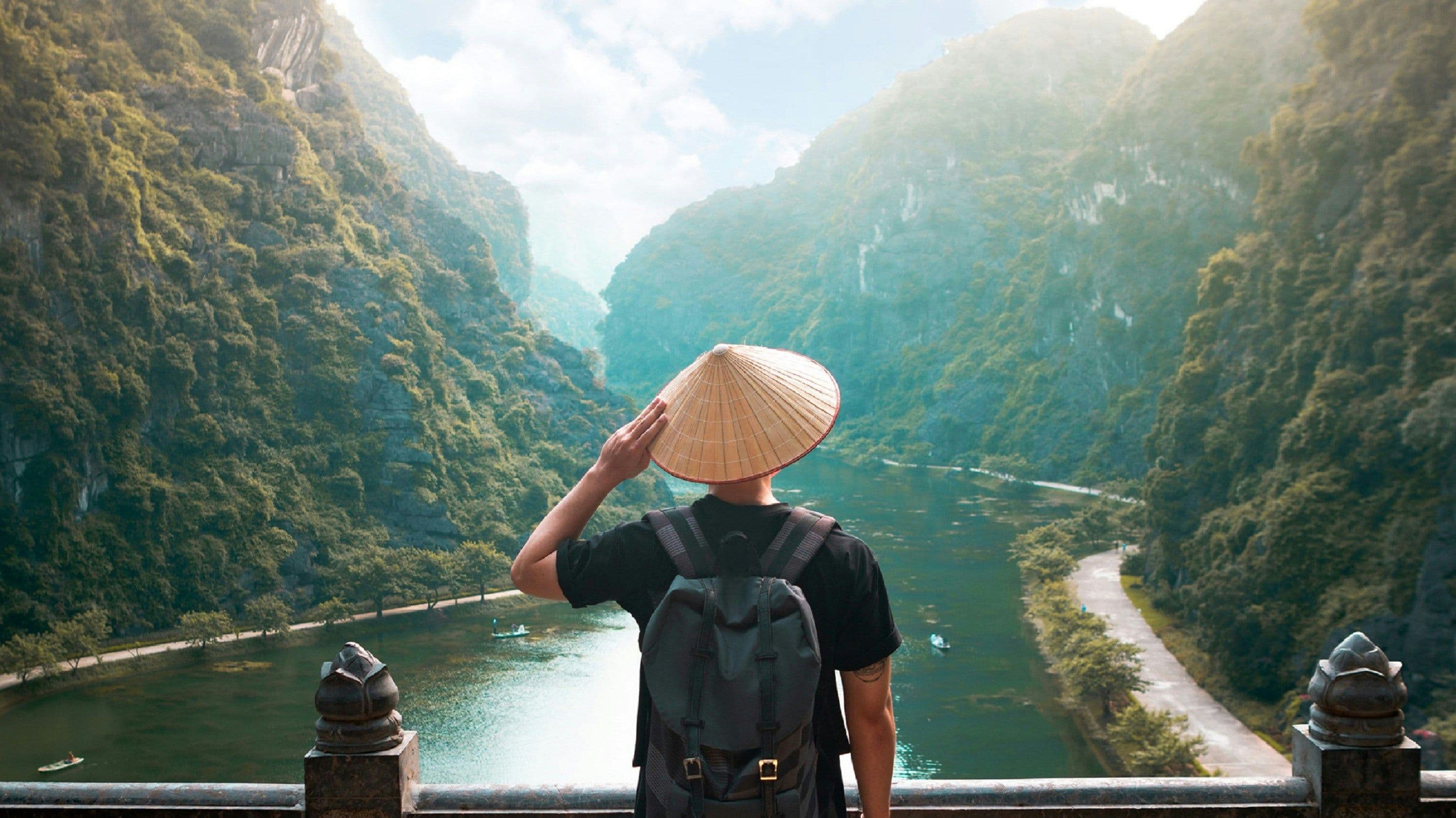 Tourist with Vietnamese hat overlooking a river surrounded by mountains in Vietnam