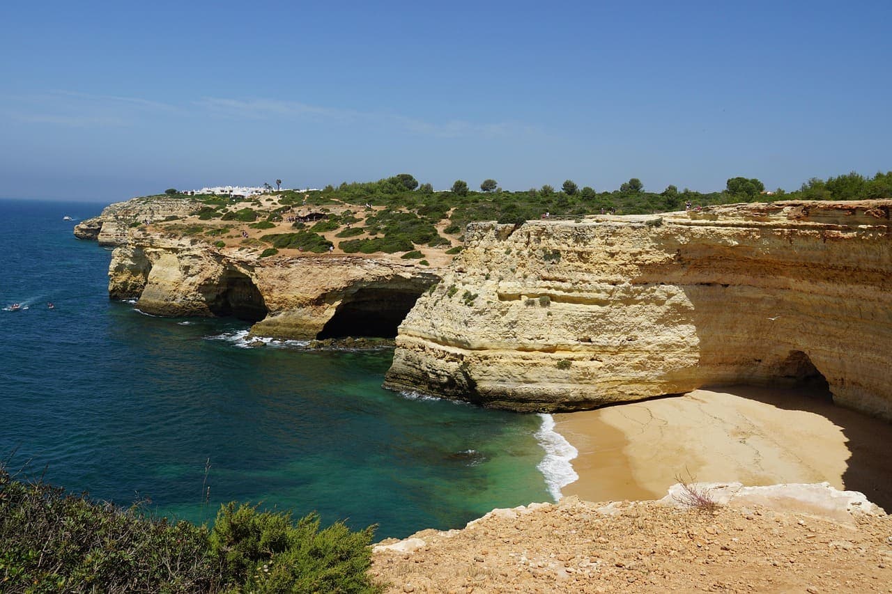 Golden limestone cliffs and sea caves along the Algarve coastline with turquoise water below.