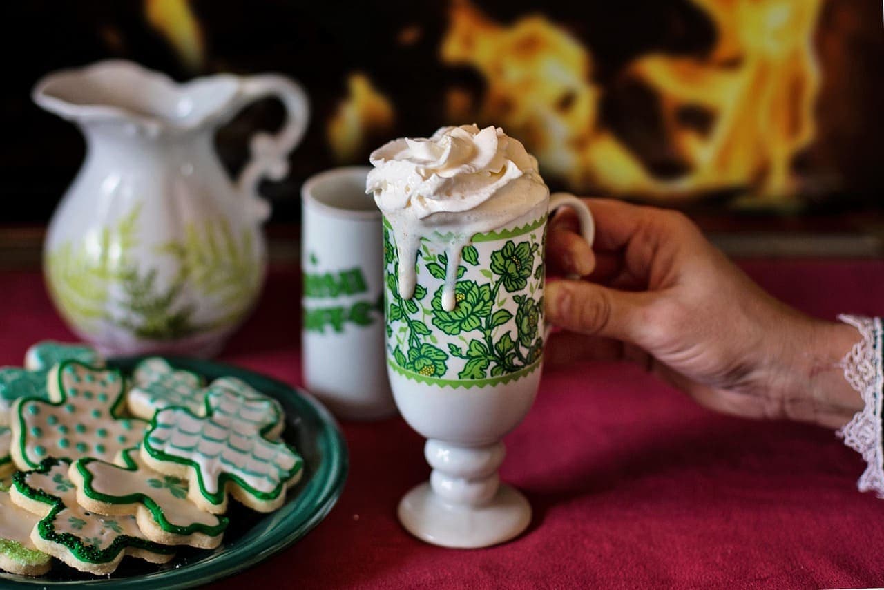 Traditional Irish coffee topped with whipped cream next to shamrock shaped biscuits on a table, symbolising St Patrick’s Festival celebrations.