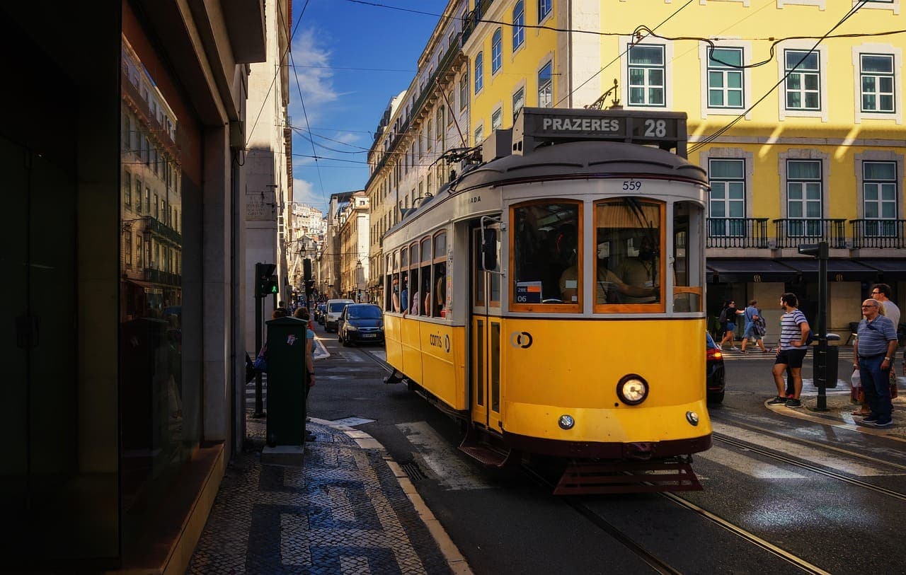 A traditional yellow Lisbon tram driving through a narrow street lined with historic buildings in the city centre.