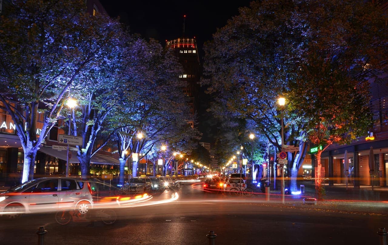 A city street in Munich at night with car light trails and illuminated trees lining the road.