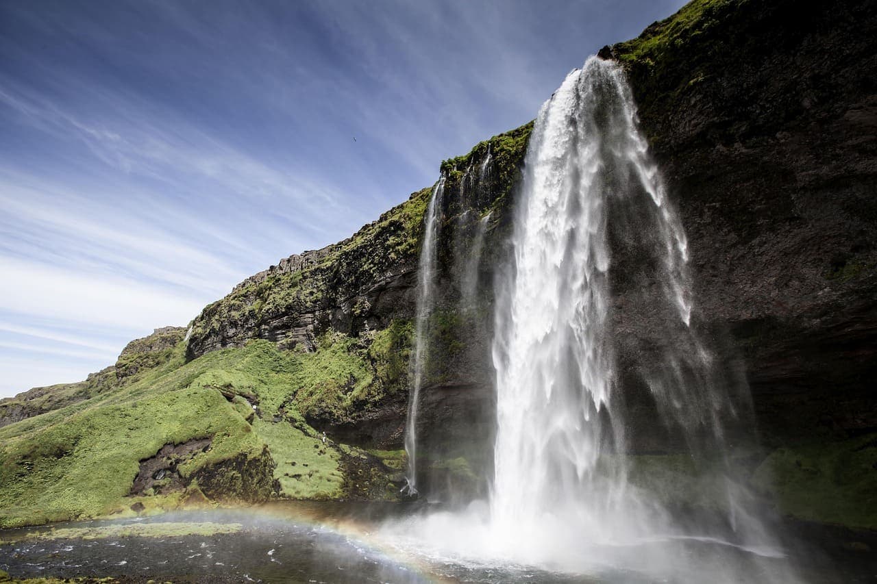 Seljalandsfoss waterfall cascading down a green moss covered cliff in South Iceland with long exposure water flow.
