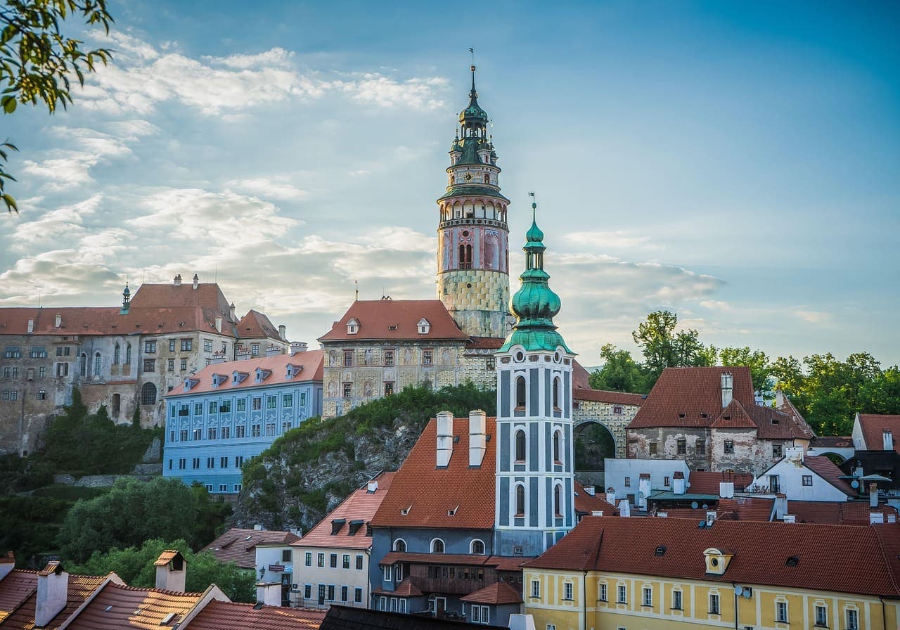 Colourful spa town buildings in Karlovy Vary with a church tower rising above the rooftops and green hills in the background.