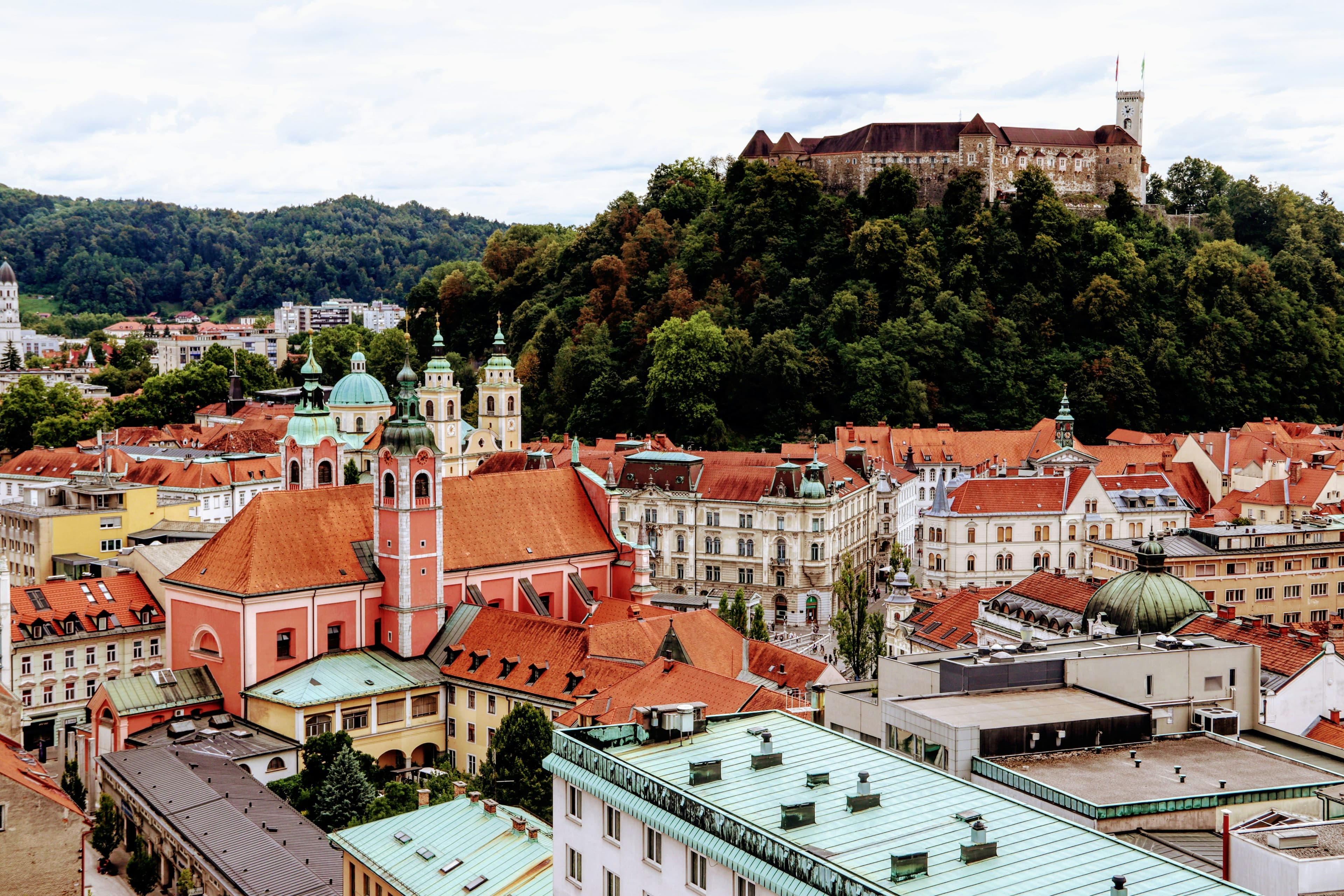 Aerial view of colorful orange roofs in Ljubljana and the green hill with castle in the distance.