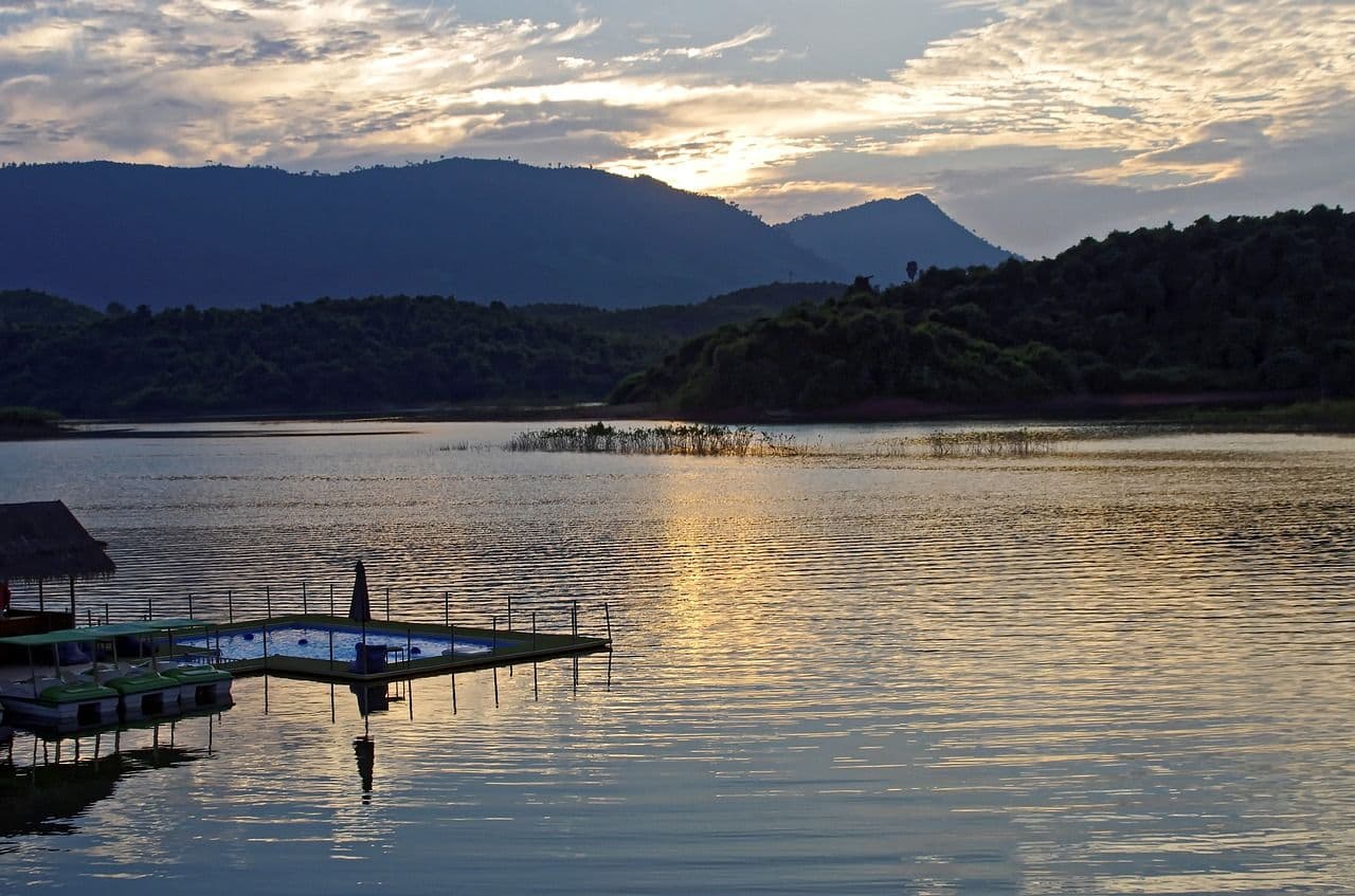 Calm river at sunset in Nong Khiaw with mountains in the background and a small wooden pier extending into the water.