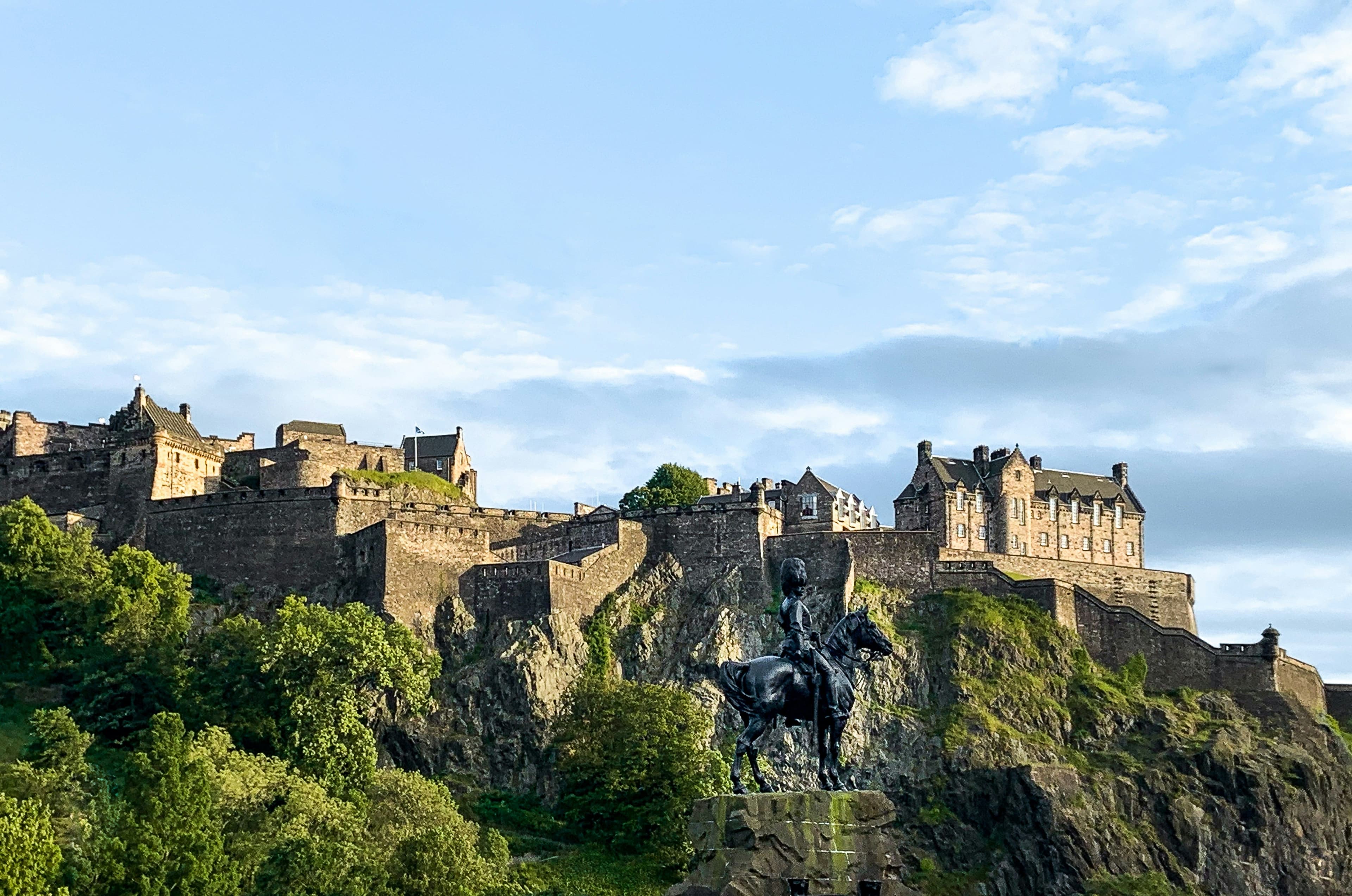 Edinburgh Castle, a big castle complex on a green mountain, on a clear day.