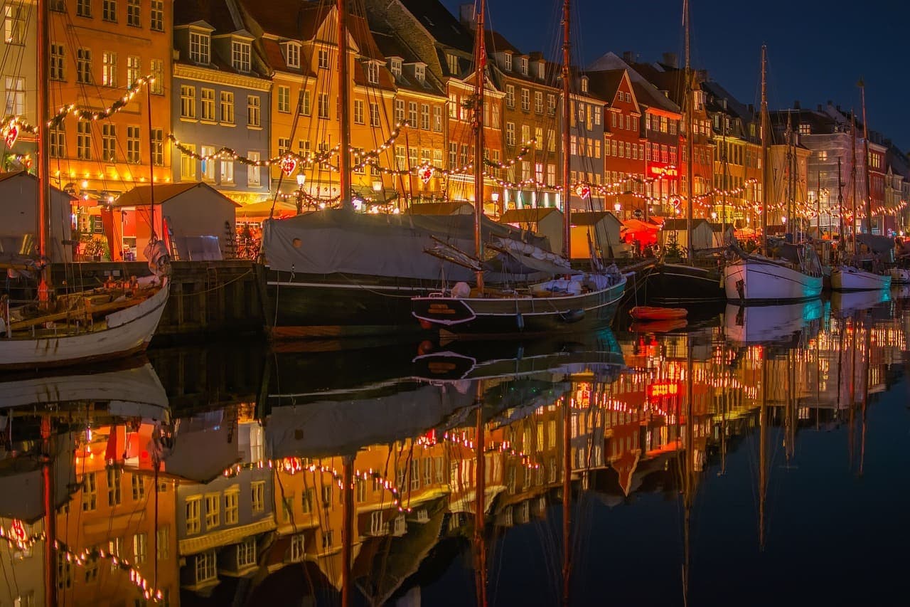 Nyhavn in Copenhagen during winter with festive lights and Christmas decorations reflected in the canal at night.