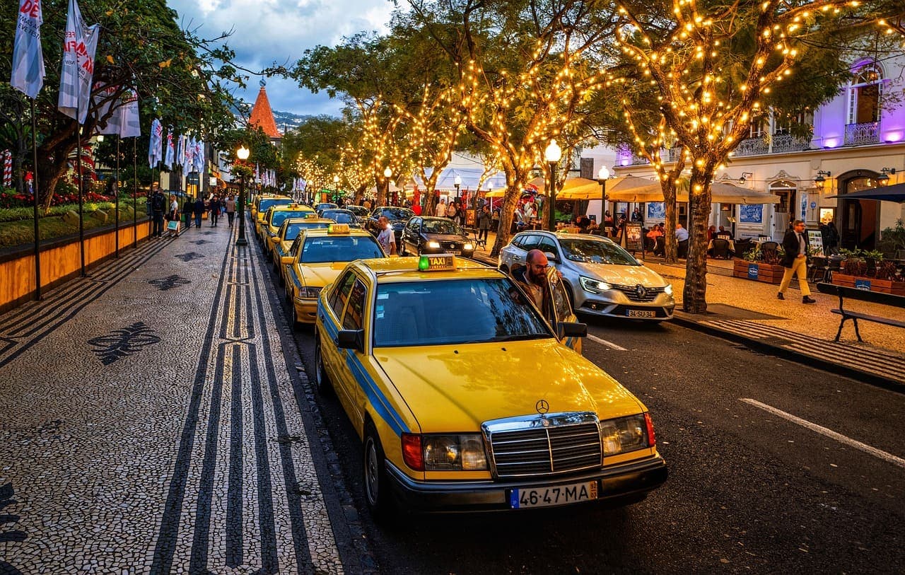A lively evening street in the Algarve with yellow taxis parked along a palm-lined road decorated with warm string lights.