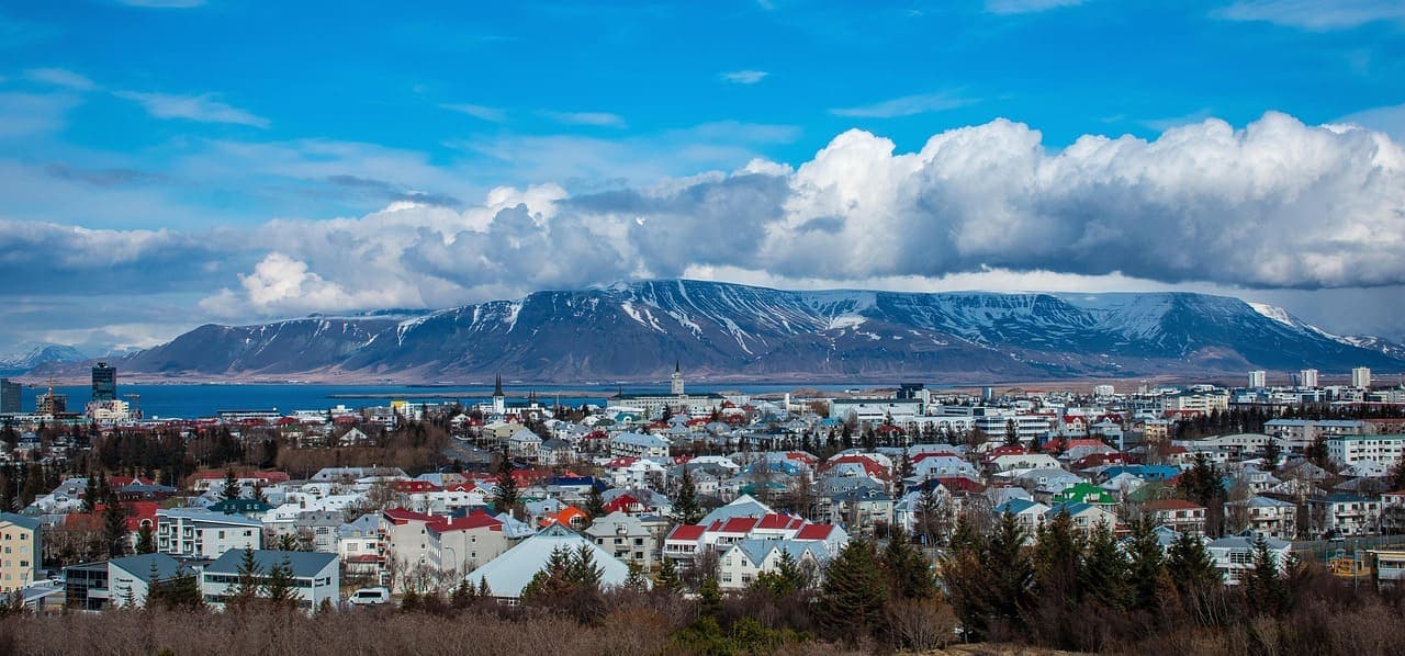 View over Reykjavik with colourful rooftops and mountains in the background under a cloudy sky.