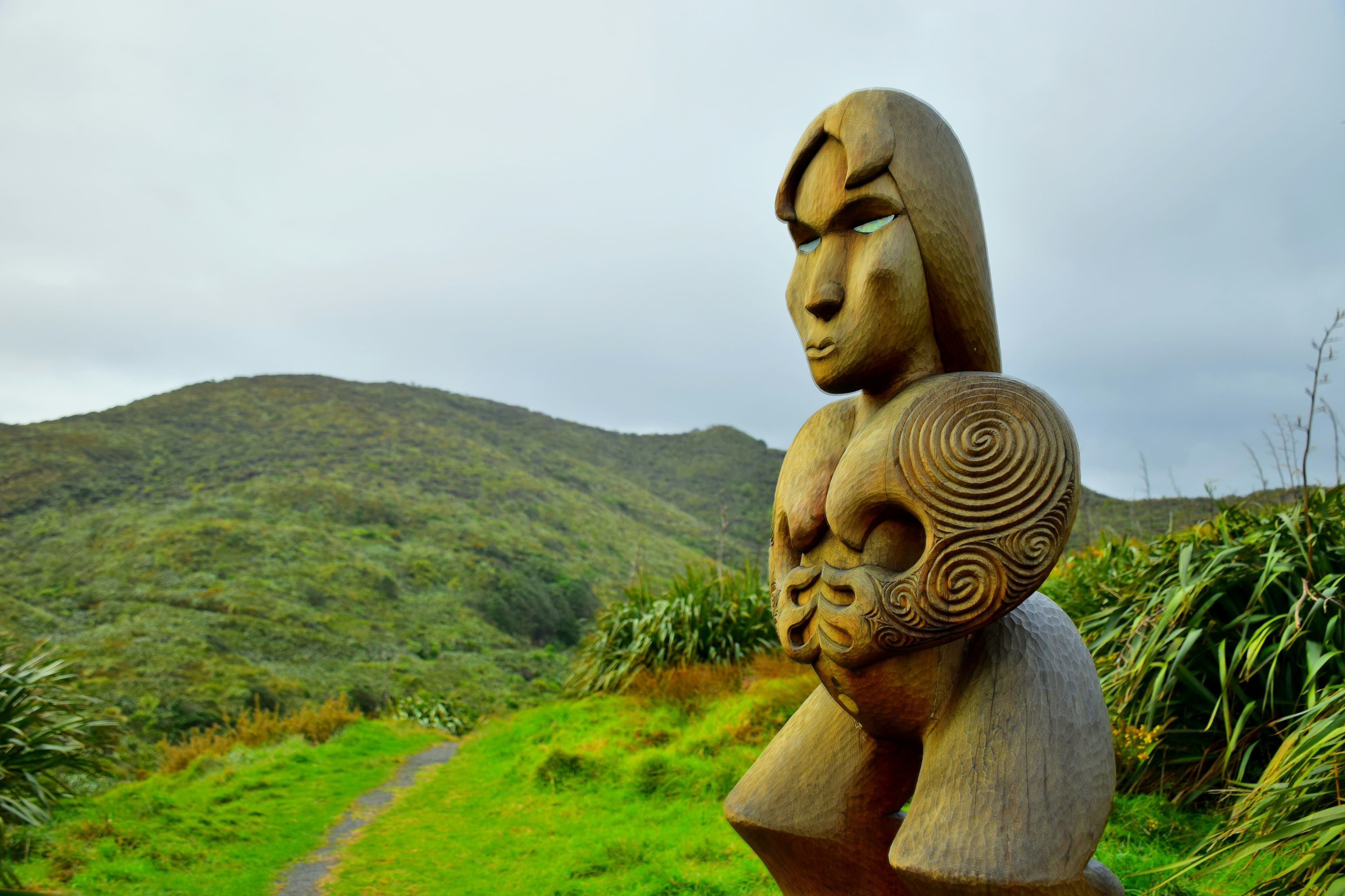 Māori statue of heads in front of a beautiful green landscape
