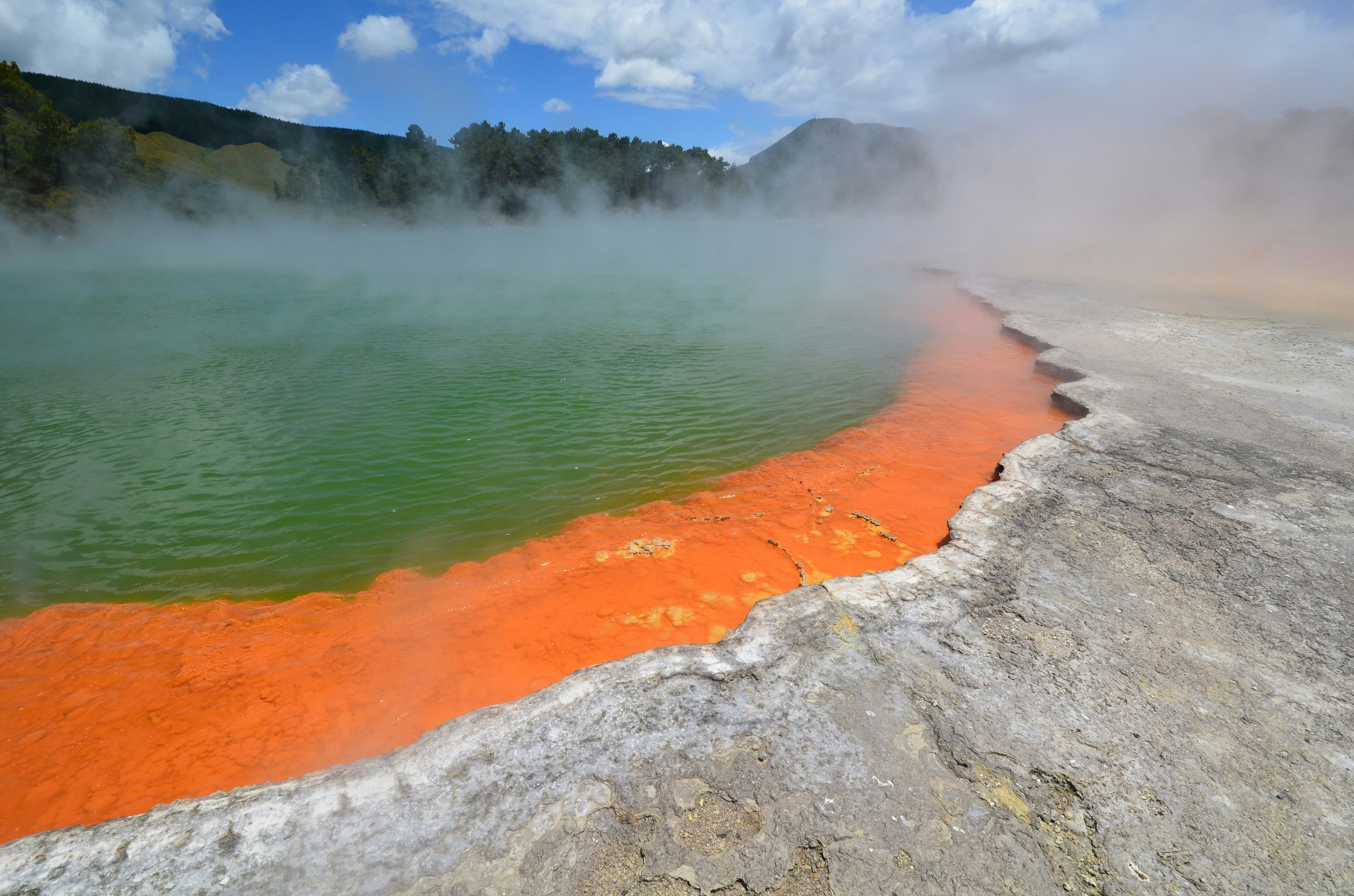 Geothermal area in Rotorua with steaming vents, bubbling pools and mountains in the background