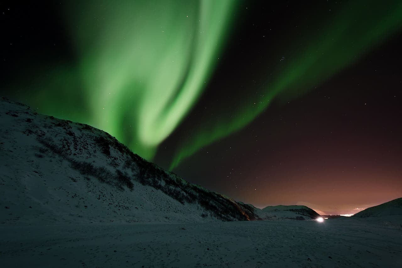 Northern lights glowing green over a snowy Icelandic landscape at night.
