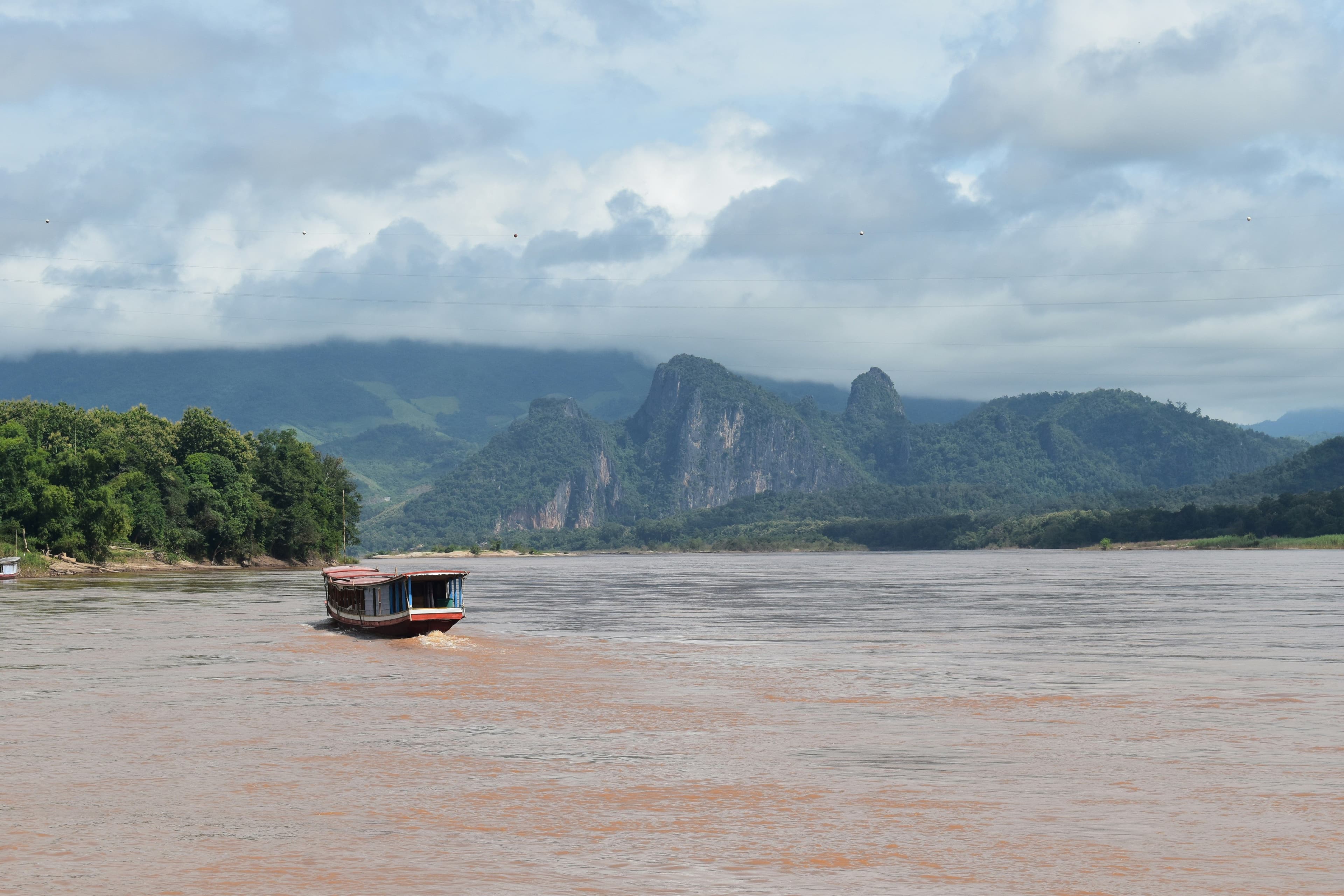 A lake with a small wooden boat in laos with mountains in the background on a cloudy rainy day