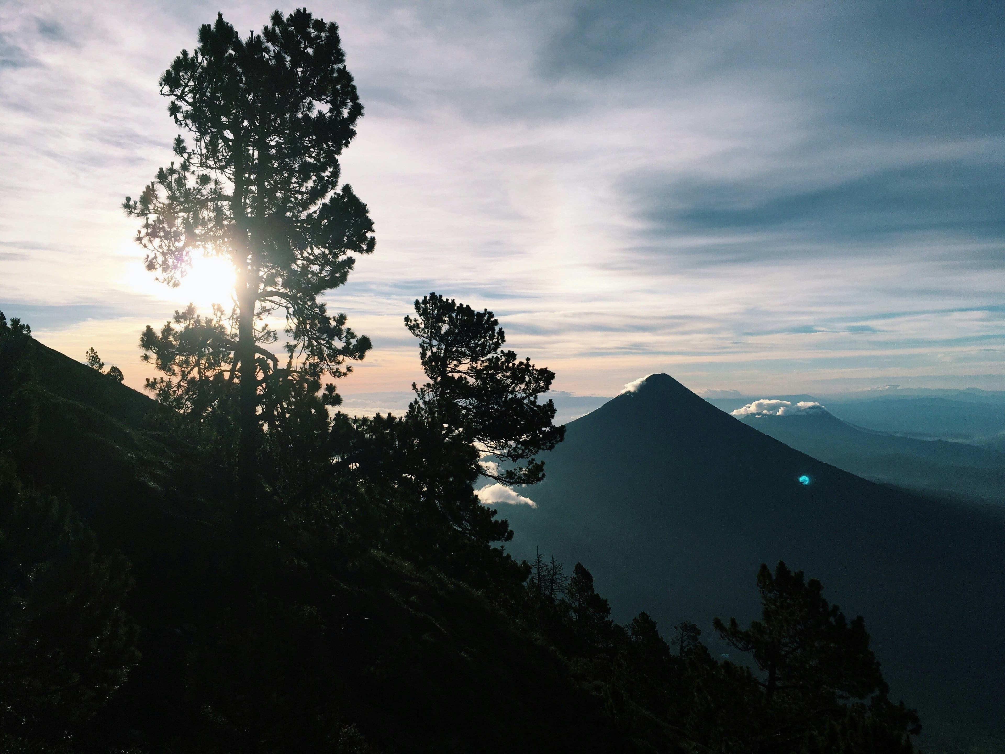 Sunrise view from a volcano hike in Guatemala, with silhouettes of trees and mountain peaks under a soft morning sky.