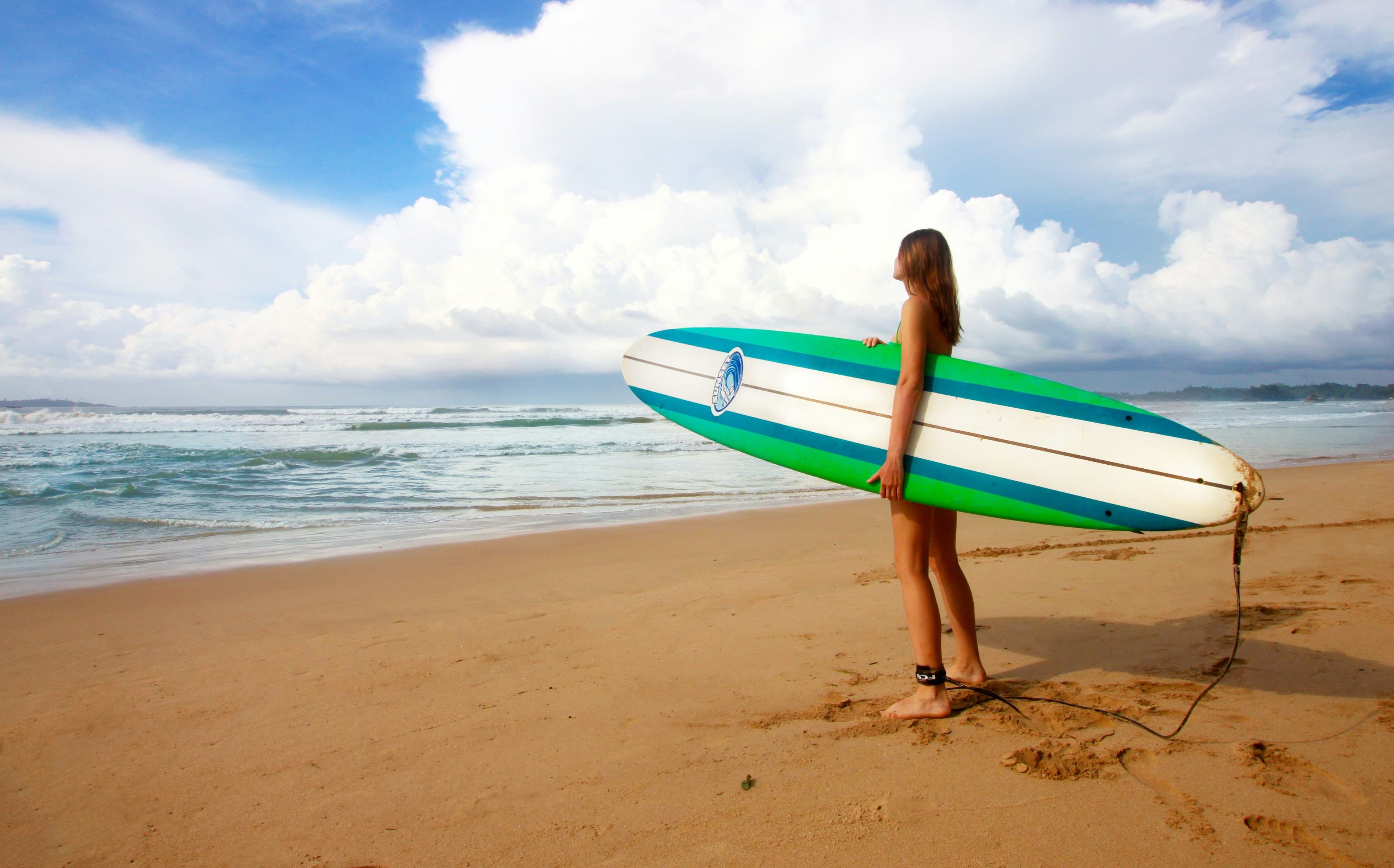 girl standing on beach holding surfboard