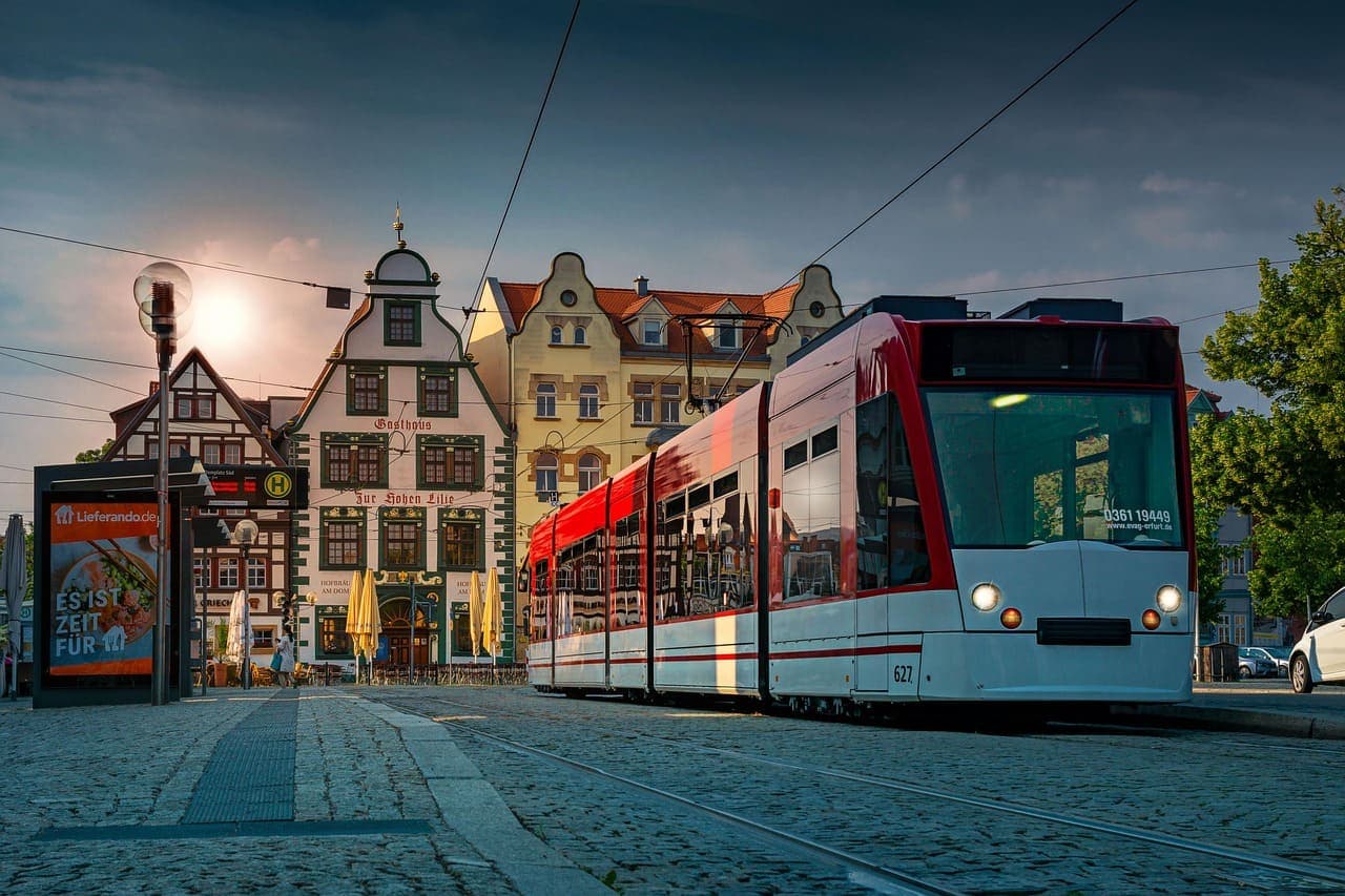 A red tram passes through a historic German town square at sunset, with colourful traditional buildings in the background.