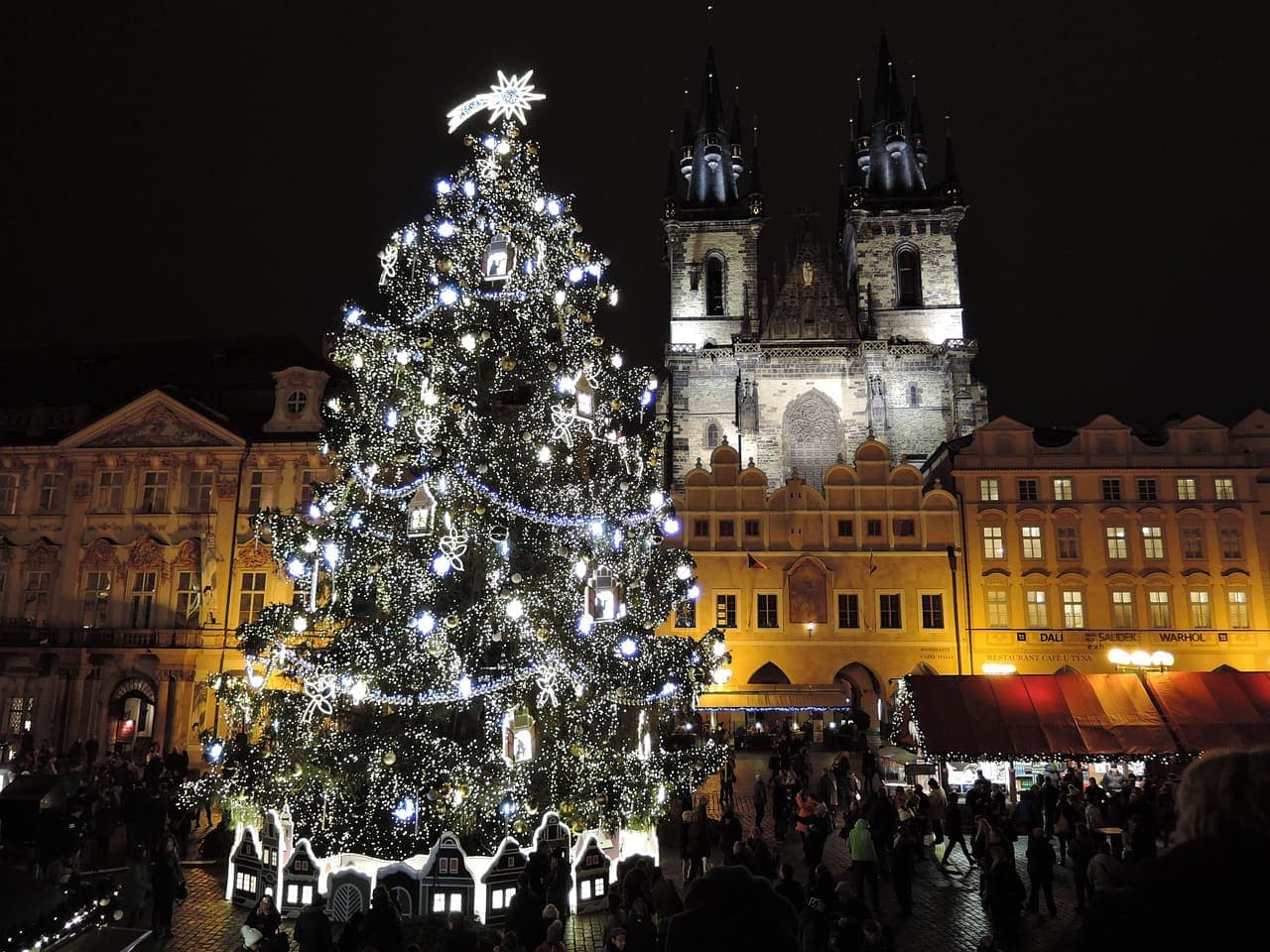 Prague Old Town Square at Christmas with a large decorated tree and festive market stalls glowing at night.