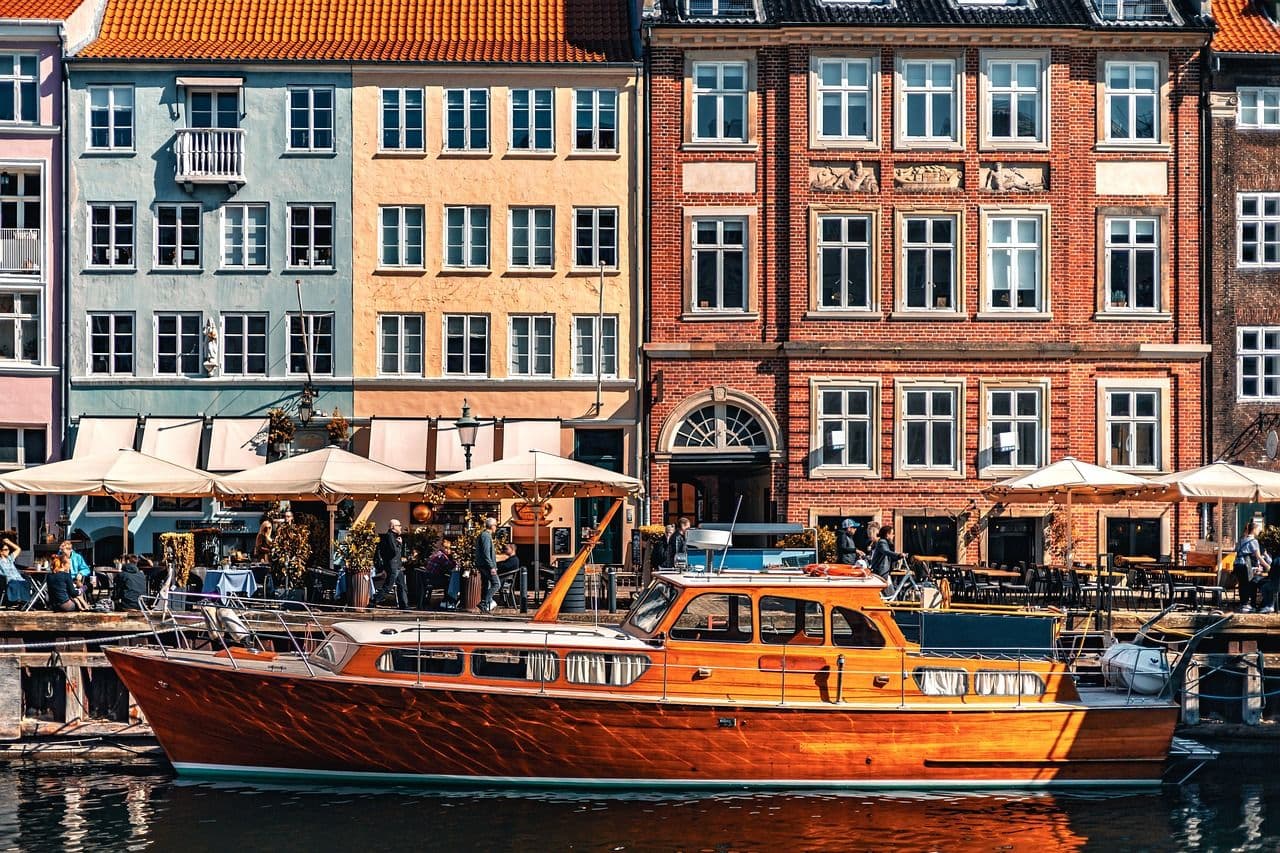 Colourful waterfront buildings in Copenhagen with outdoor cafés and a boat in the canal, creating a lively and scenic city atmosphere.