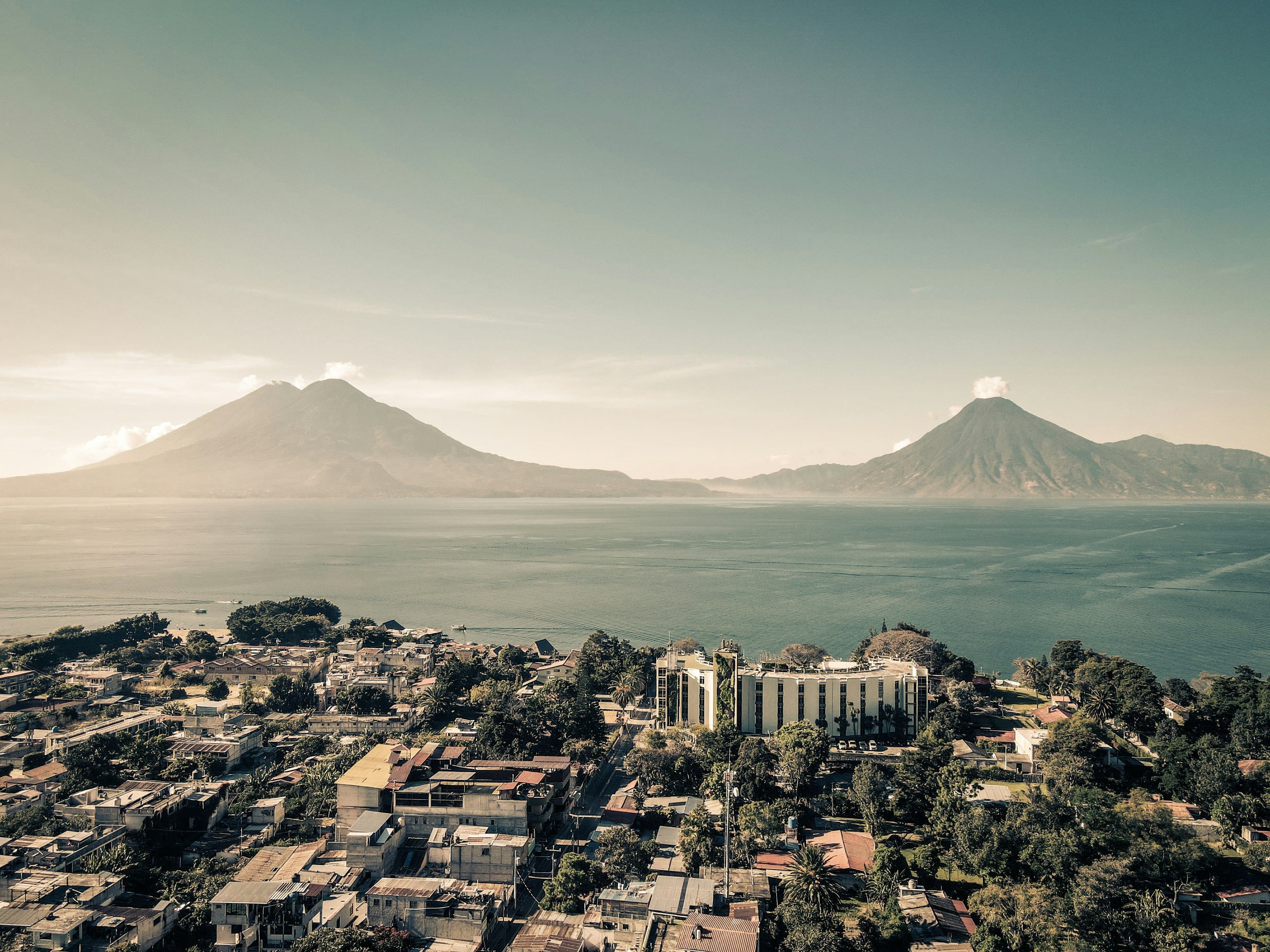 View over Lake Atitlán with two volcanoes in the background and a town along the lakeshore under soft light.