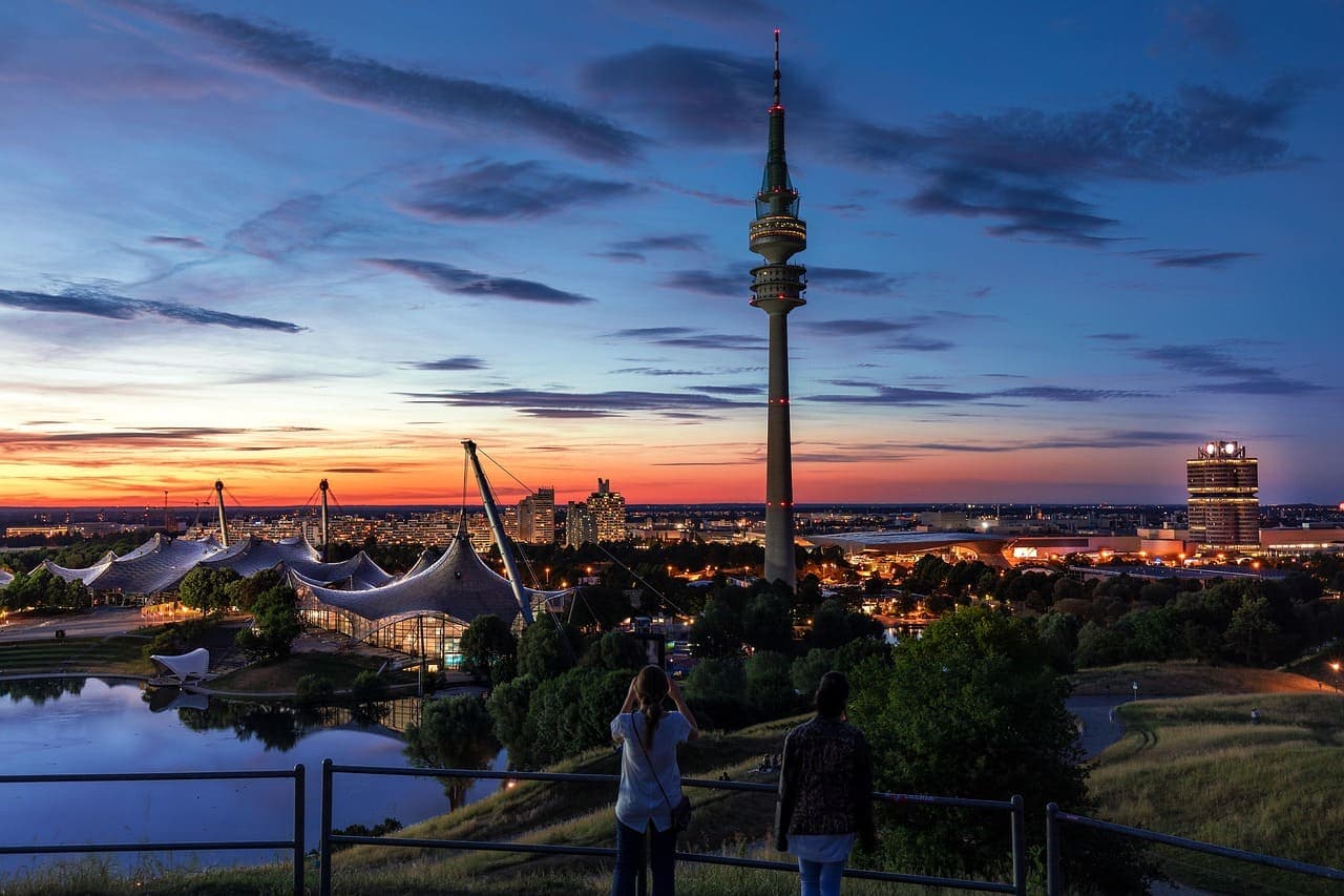 Munich skyline at dusk with the Olympic Tower and Olympic Park visible under a colourful evening sky.