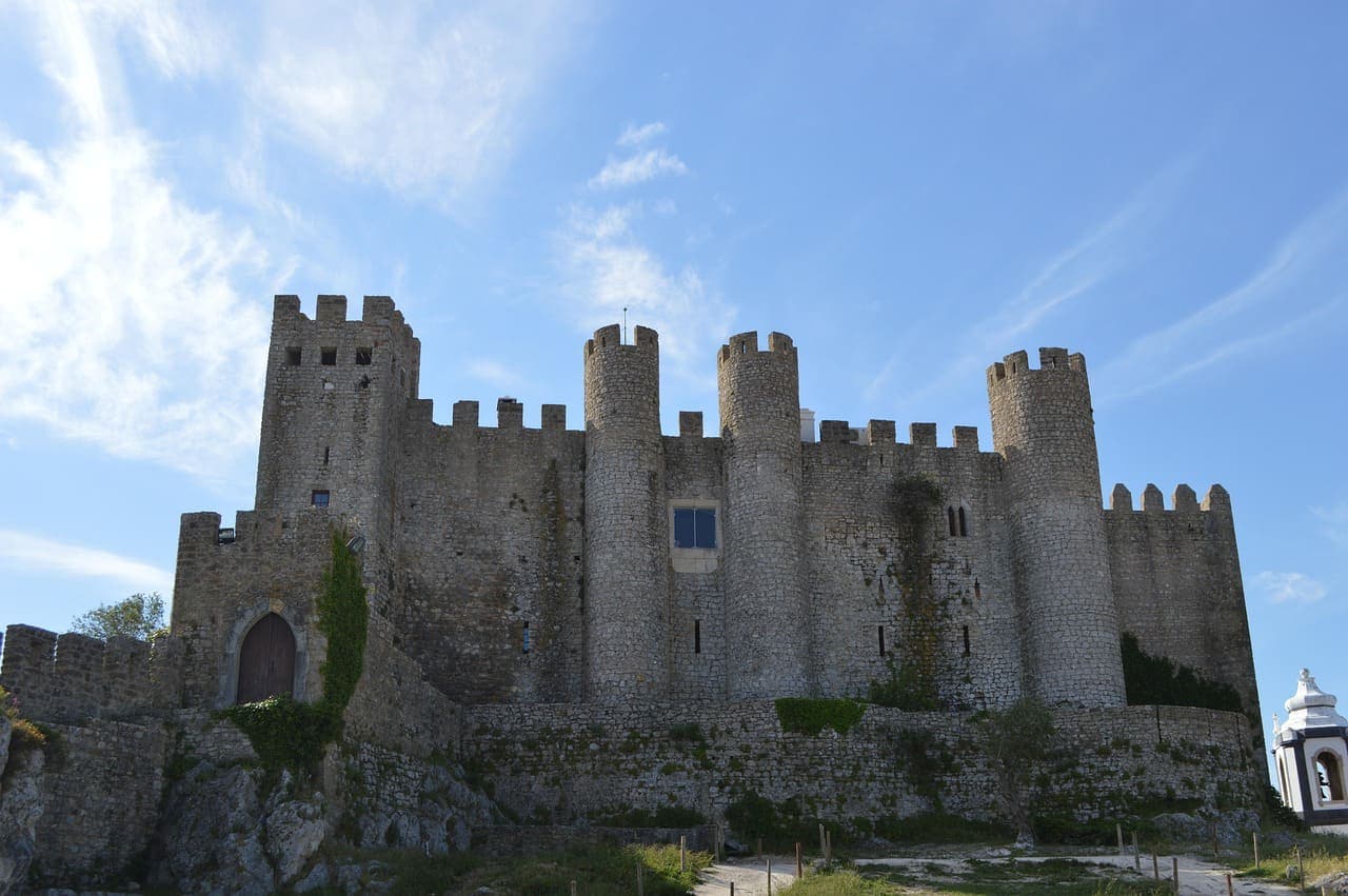 Medieval stone castle in Óbidos with high walls and towers against a bright blue sky.